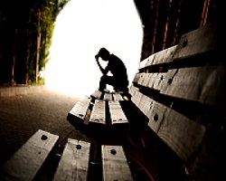 Man sitting on a bench, holding his head in his hands.